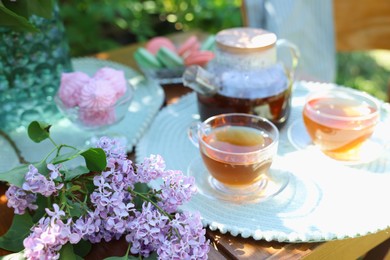 Photo of Beautiful lilac flowers, sweets and tea on wooden table in garden, closeup