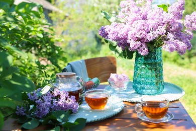 Photo of Beautiful lilac flowers, sweets and tea on wooden table in garden