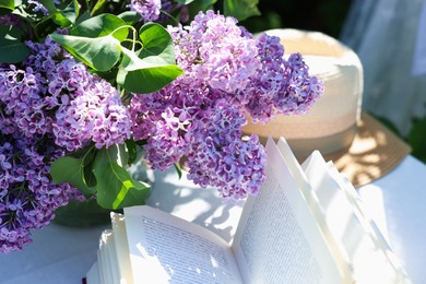 Photo of Beautiful lilac flowers, book and straw hat on table in garden, closeup