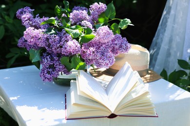 Photo of Beautiful lilac flowers, book and straw hat on table in garden