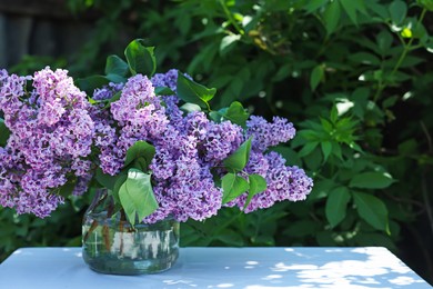 Photo of Beautiful lilac flowers in vase on table in garden