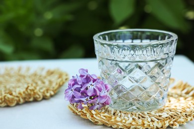 Photo of Beautiful lilac flowers and glass on table in garden, closeup. Space for text