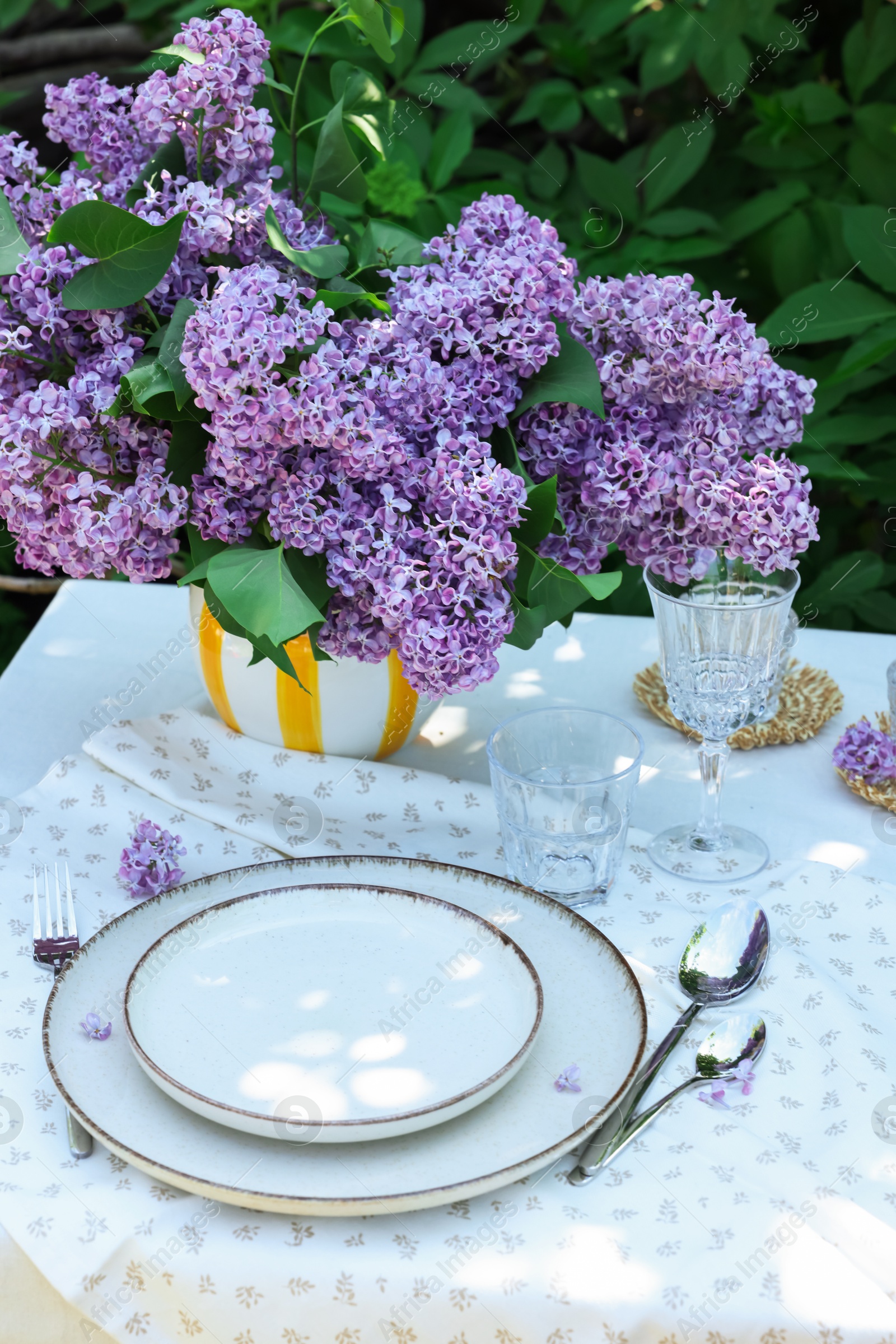 Beautiful lilac flowers, plates, cutlery and glasses on table in garden Photo of Beautiful lilac flowers, plates, cutlery and glasses on table in garden