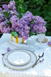 Photo of Beautiful lilac flowers, plates, cutlery and glasses on table in garden