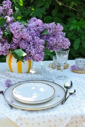 Photo of Beautiful lilac flowers, plates, cutlery, glasses and candles on table in garden