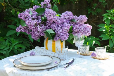 Photo of Beautiful lilac flowers, plates, cutlery, glasses and candles on table in garden