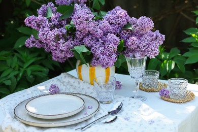 Photo of Beautiful lilac flowers, plates, cutlery, glasses and candles on table in garden
