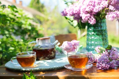 Photo of Beautiful lilac flowers, tea and zephyrs on wooden table in garden