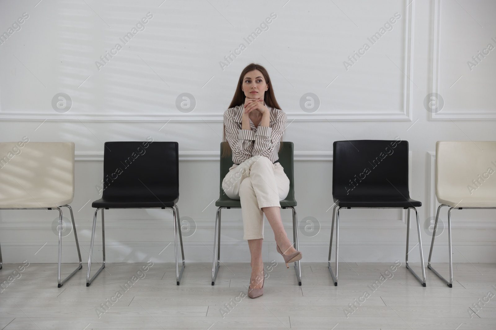 Woman sitting on chair and waiting for appointment indoors Photo of Woman sitting on chair and waiting for appointment indoors