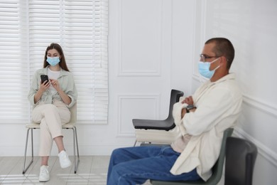 Photo of Man and woman in medical masks waiting for appointment indoors, selective focus
