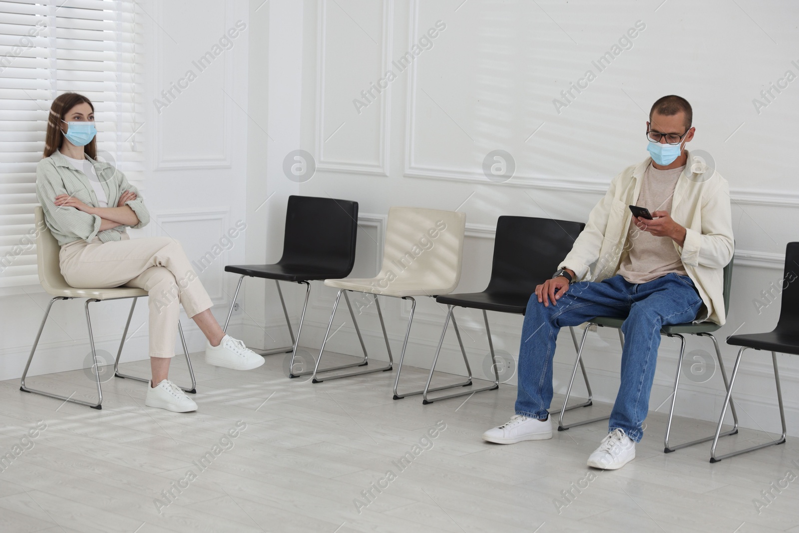 Man and woman in medical masks waiting for appointment indoors Photo of Man and woman in medical masks waiting for appointment indoors