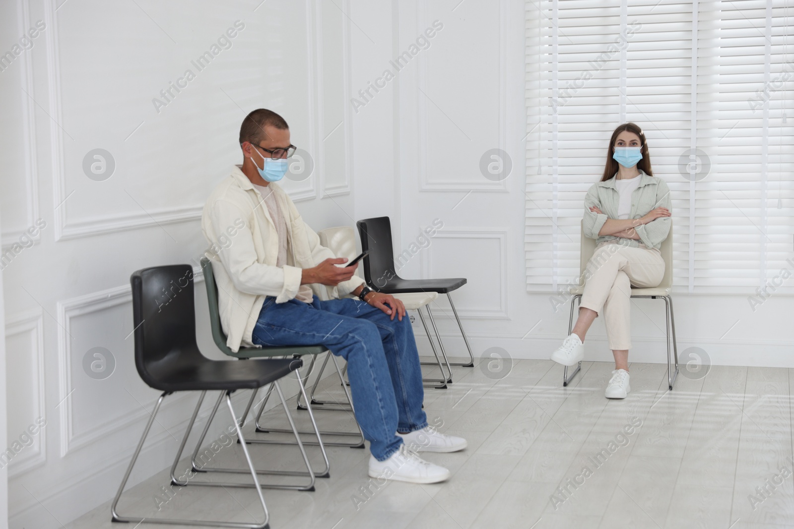 Man and woman in medical masks waiting for appointment indoors Photo of Man and woman in medical masks waiting for appointment indoors