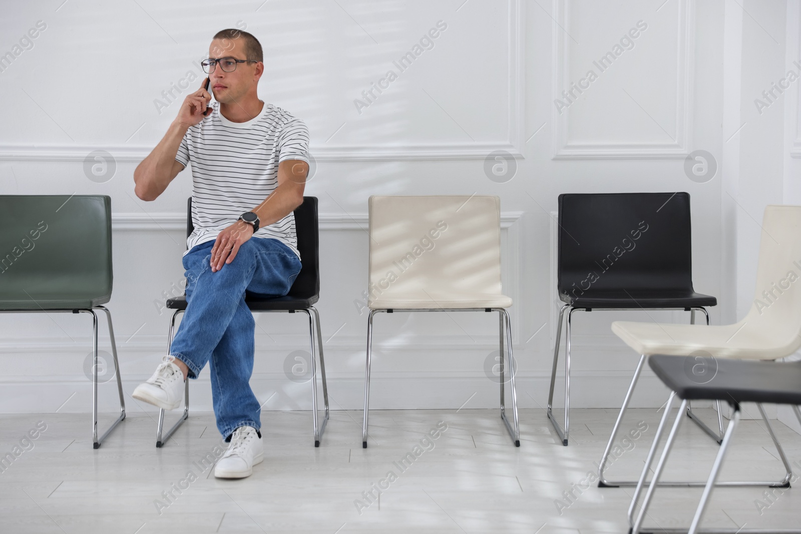 Man talking on smartphone while waiting for appointment indoors Photo of Man talking on smartphone while waiting for appointment indoors