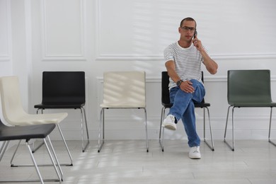 Photo of Man talking on smartphone while waiting for appointment indoors
