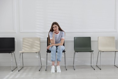 Photo of Woman sitting on chair and waiting for appointment indoors