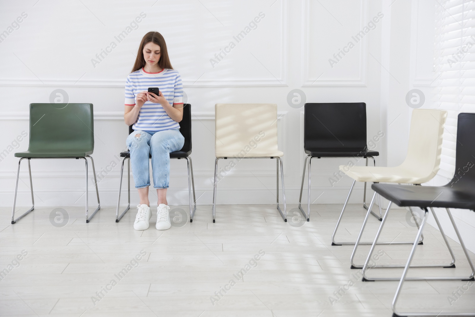 Woman with smartphone waiting for appointment indoors Photo of Woman with smartphone waiting for appointment indoors