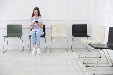 Photo of Woman with smartphone waiting for appointment indoors