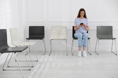 Photo of Woman with smartphone waiting for appointment indoors