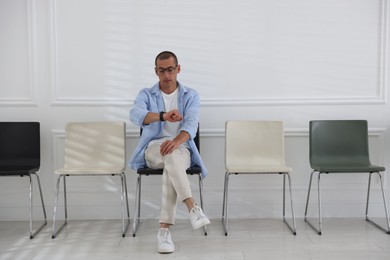Photo of Man looking at wristwatch while waiting for appointment indoors