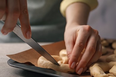 Photo of Woman cutting uncooked pretzel at table, closeup