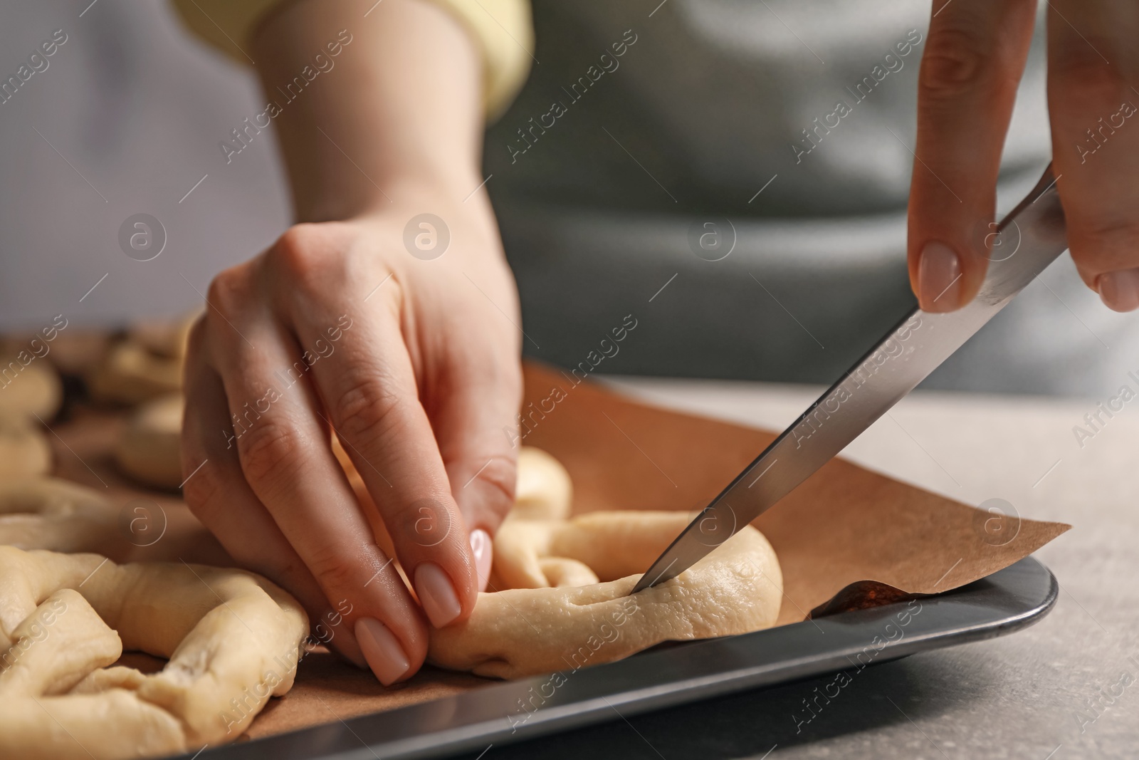 Woman cutting uncooked pretzel at grey table, closeup Photo of Woman cutting uncooked pretzel at grey table, closeup