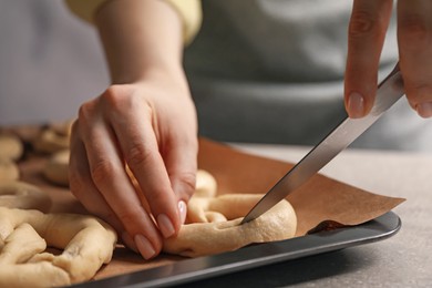 Photo of Woman cutting uncooked pretzel at grey table, closeup