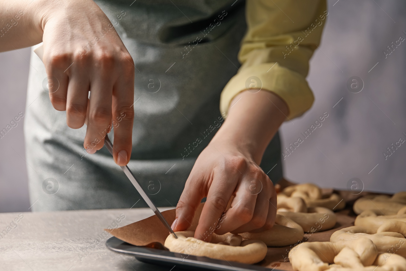 Woman cutting uncooked pretzel at grey table, closeup Photo of Woman cutting uncooked pretzel at grey table, closeup