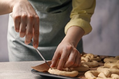 Photo of Woman cutting uncooked pretzel at grey table, closeup