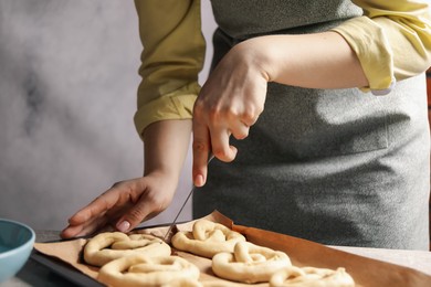 Photo of Woman cutting uncooked pretzel at table, closeup
