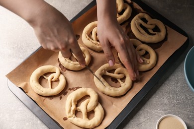 Photo of Woman cutting uncooked pretzel at grey table, above view