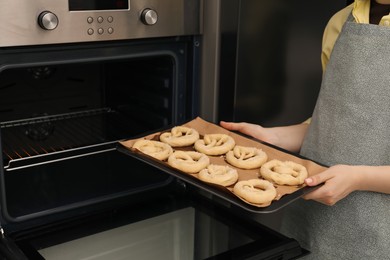 Photo of Woman putting baking dish with uncooked pretzels into oven, closeup