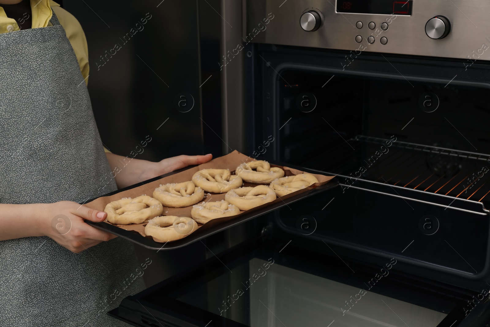 Woman putting baking dish with uncooked pretzels into oven, closeup Photo of Woman putting baking dish with uncooked pretzels into oven, closeup