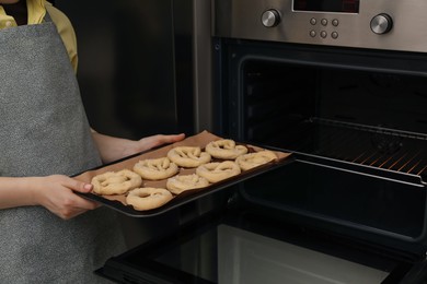 Photo of Woman putting baking dish with uncooked pretzels into oven, closeup