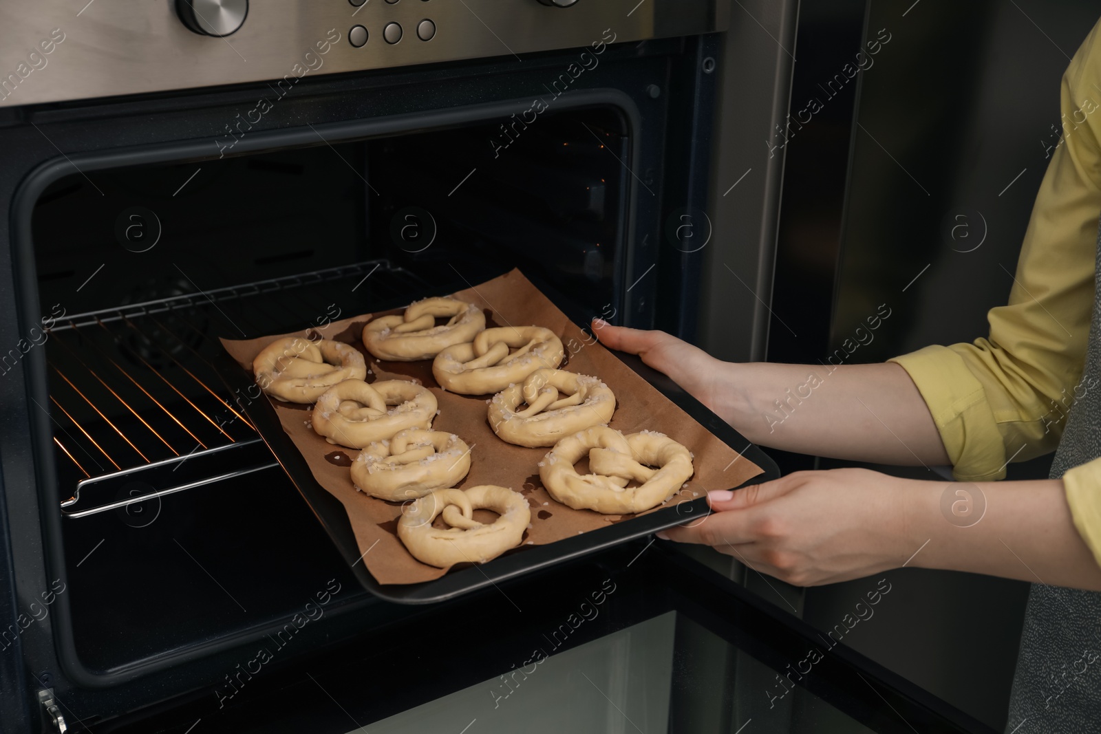Woman putting baking dish with uncooked pretzels into oven, closeup Photo of Woman putting baking dish with uncooked pretzels into oven, closeup