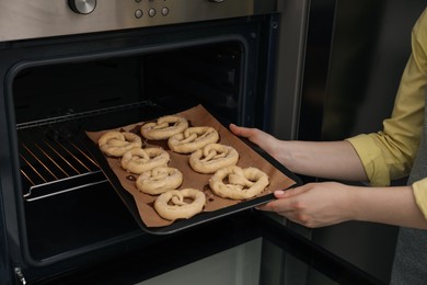 Photo of Woman putting baking dish with uncooked pretzels into oven, closeup