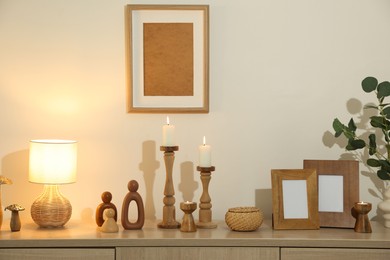 Photo of Stylish candlesticks with burning candles and other decor on cabinet near beige wall indoors
