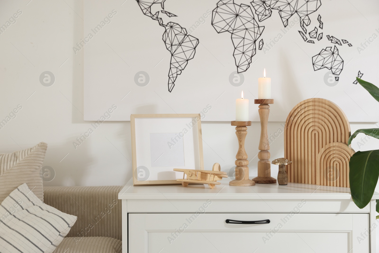 Stylish candlesticks with burning candles and other decor on cabinet near wall indoors Photo of Stylish candlesticks with burning candles and other decor on cabinet near wall indoors