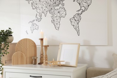 Photo of Stylish candlesticks with burning candles and other decor on cabinet near wall indoors