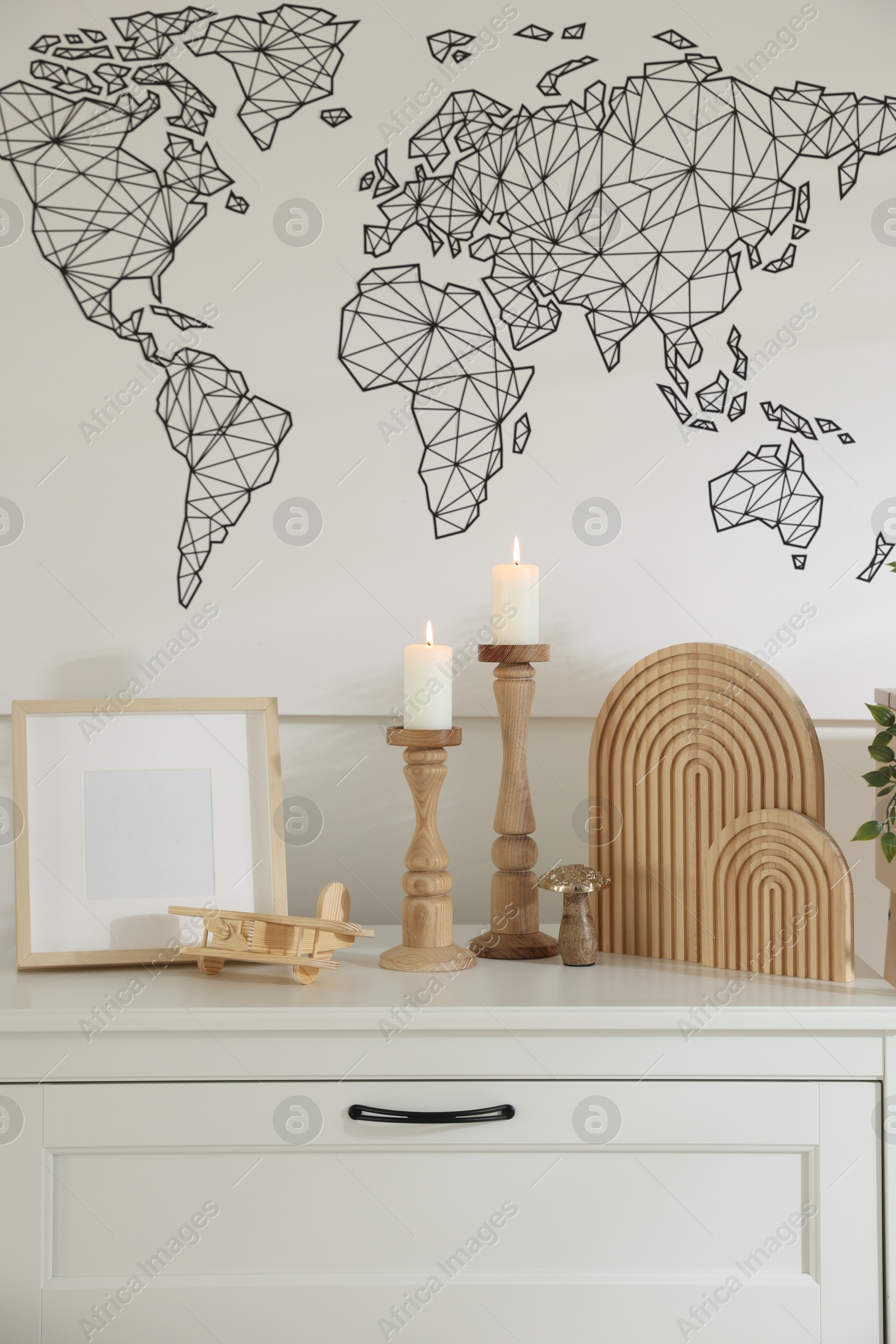 Stylish candlesticks with burning candles and other decor on cabinet near wall indoors Photo of Stylish candlesticks with burning candles and other decor on cabinet near wall indoors