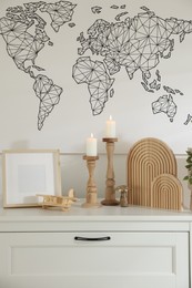 Photo of Stylish candlesticks with burning candles and other decor on cabinet near wall indoors