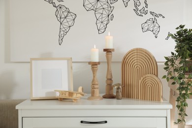 Photo of Stylish candlesticks with burning candles and other decor on cabinet near wall indoors