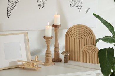 Photo of Stylish candlesticks with burning candles and other decor on cabinet near wall indoors
