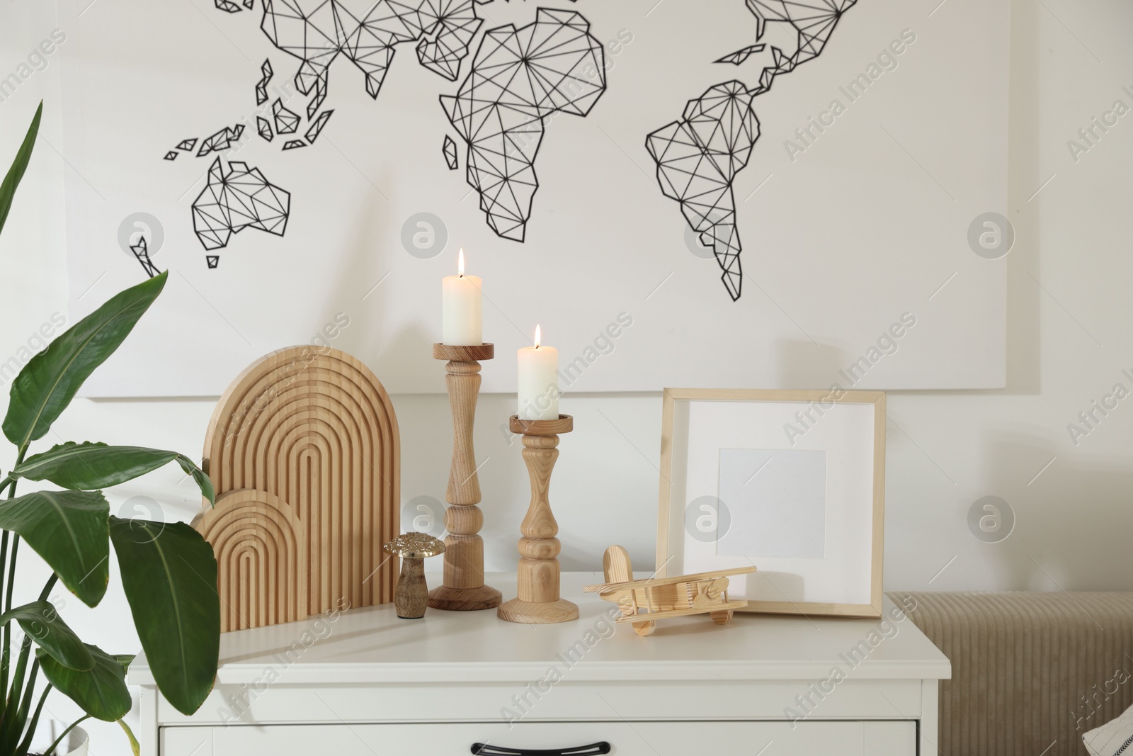 Stylish candlesticks with burning candles and other decor on cabinet near wall indoors Photo of Stylish candlesticks with burning candles and other decor on cabinet near wall indoors