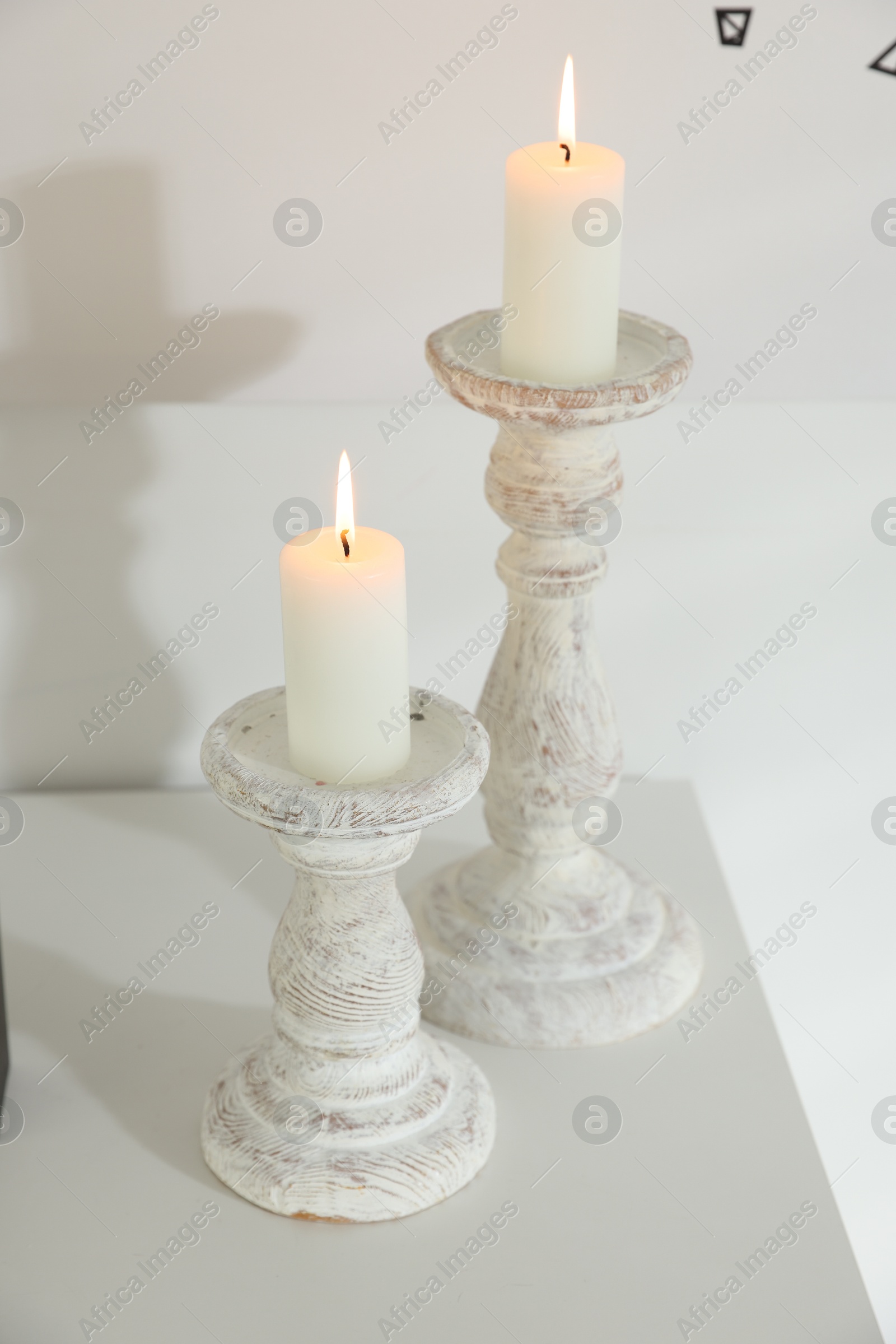 Photo of Stylish candlesticks with burning candles on table near white wall indoors, closeup