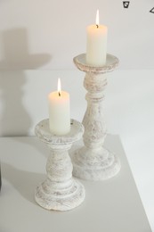 Photo of Stylish candlesticks with burning candles on table near white wall indoors, closeup
