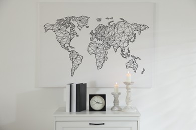 Photo of Stylish candlesticks with burning candles, alarm clock and books on cabinet near white wall indoors