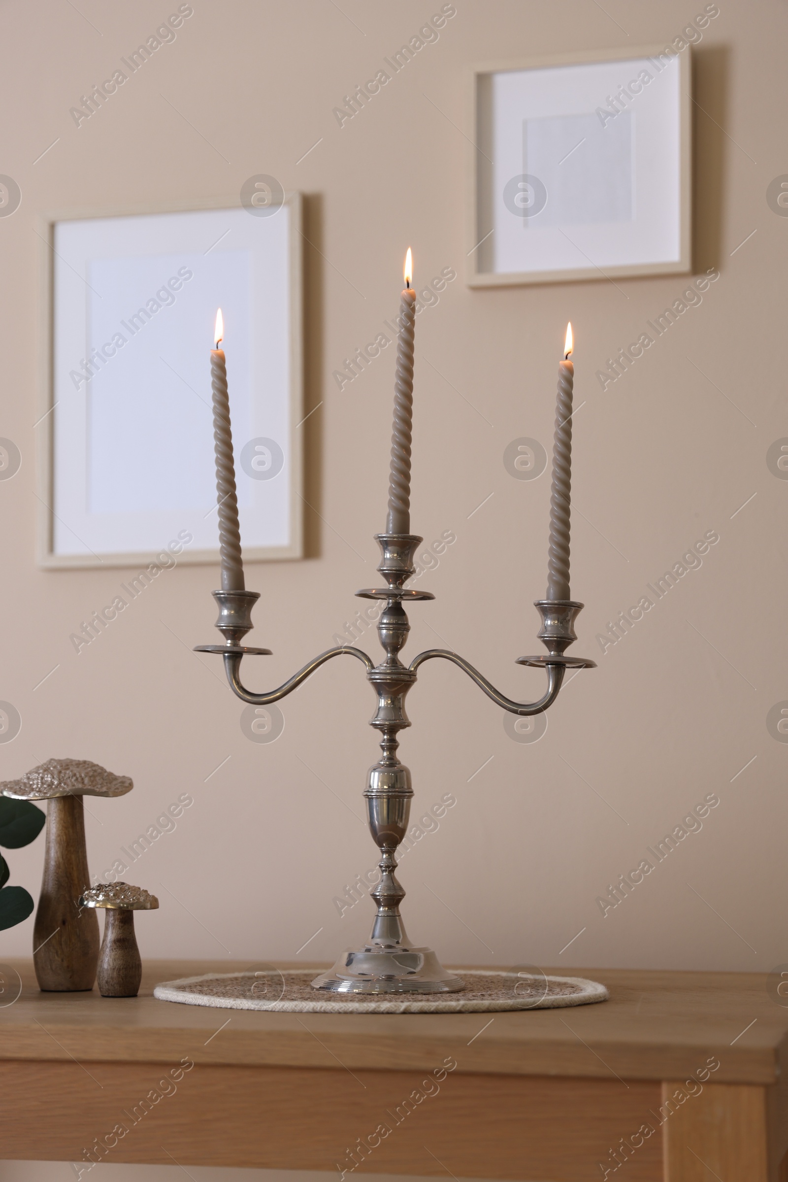 Stylish candlestick with burning candles and other decor on wooden table near beige wall indoors Photo of Stylish candlestick with burning candles and other decor on wooden table near beige wall indoors