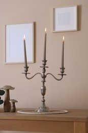 Photo of Stylish candlestick with burning candles and other decor on wooden table near beige wall indoors