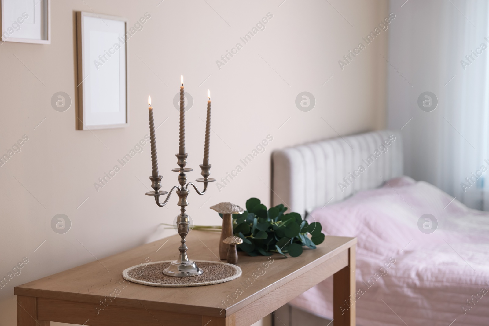 Stylish candlestick with burning candles and other decor on wooden table near beige wall indoors Photo of Stylish candlestick with burning candles and other decor on wooden table near beige wall indoors