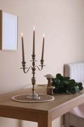 Photo of Stylish candlestick with burning candles and other decor on wooden table near beige wall indoors